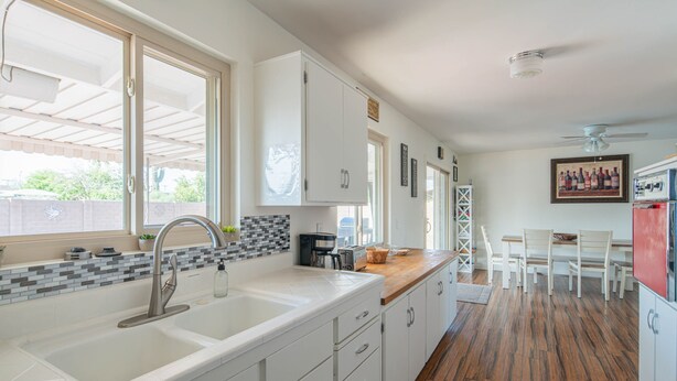 A kitchen with a large white sink, white cabinets, a wooden countertop, and a dining area with white chairs and a table.