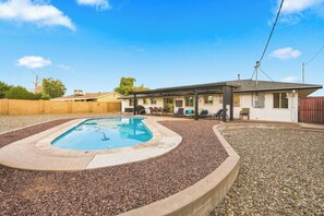 Une piscine avec un espace patio, un coin salon couvert et un bâtiment doté d’un toit plat.