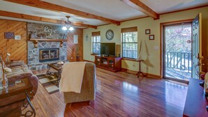 A cozy living room with a stone fireplace, wooden beams, a television, and a large window overlooking a deck. - Quaint, Spacious, And Minutes From Everything You Want To See In Chattanooga (Chattanooga)