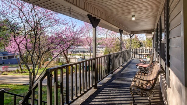 A covered porch with a bench and railing, overlooking a street with blooming trees. - Quaint, Spacious, And Minutes From Everything You Want To See In Chattanooga (Chattanooga)