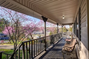 A covered porch with a bench and railing, overlooking a street with blooming trees.
