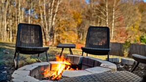 A fire pit with three chairs around it, set in a backyard with trees in the background.