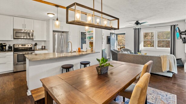 A modern kitchen with white cabinets, stainless steel appliances, a wooden dining table, and a central island with bar stools.