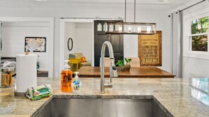 A modern kitchen with a stainless steel sink, a hanging light fixture, and a wooden sign on the wall.