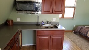 A kitchen with wooden cabinets, a stainless steel sink, and a microwave. - Large Brighton area studio  (Brighton)