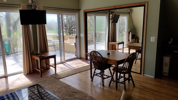 A room with a wooden dining table, two chairs, a TV on the wall, and a sliding glass door leading to an outdoor area. - Large Brighton area studio  (Brighton)