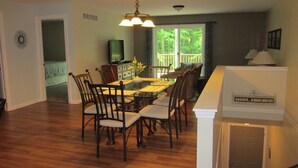 A dining area with a wooden table and chairs, a television, and a view of the outdoors through large windows. - 2 Bedroom, Full Kitchen, Dining Room, Living Room, Large Deck, Jacuzzi -Sleeps 8 (Benzonia)