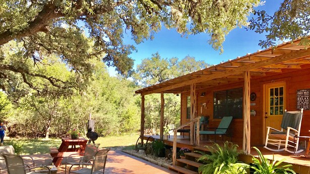A wooden cabin with a porch, outdoor seating, and a barbecue grill.