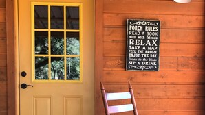 A wooden door with a yellow frame and a window, a rocking chair with a red cushion, and a sign with porch rules.