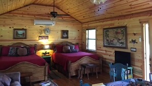 A cabin with two wooden beds, a ceiling fan, a mounted air conditioner, and a painting on the wall.