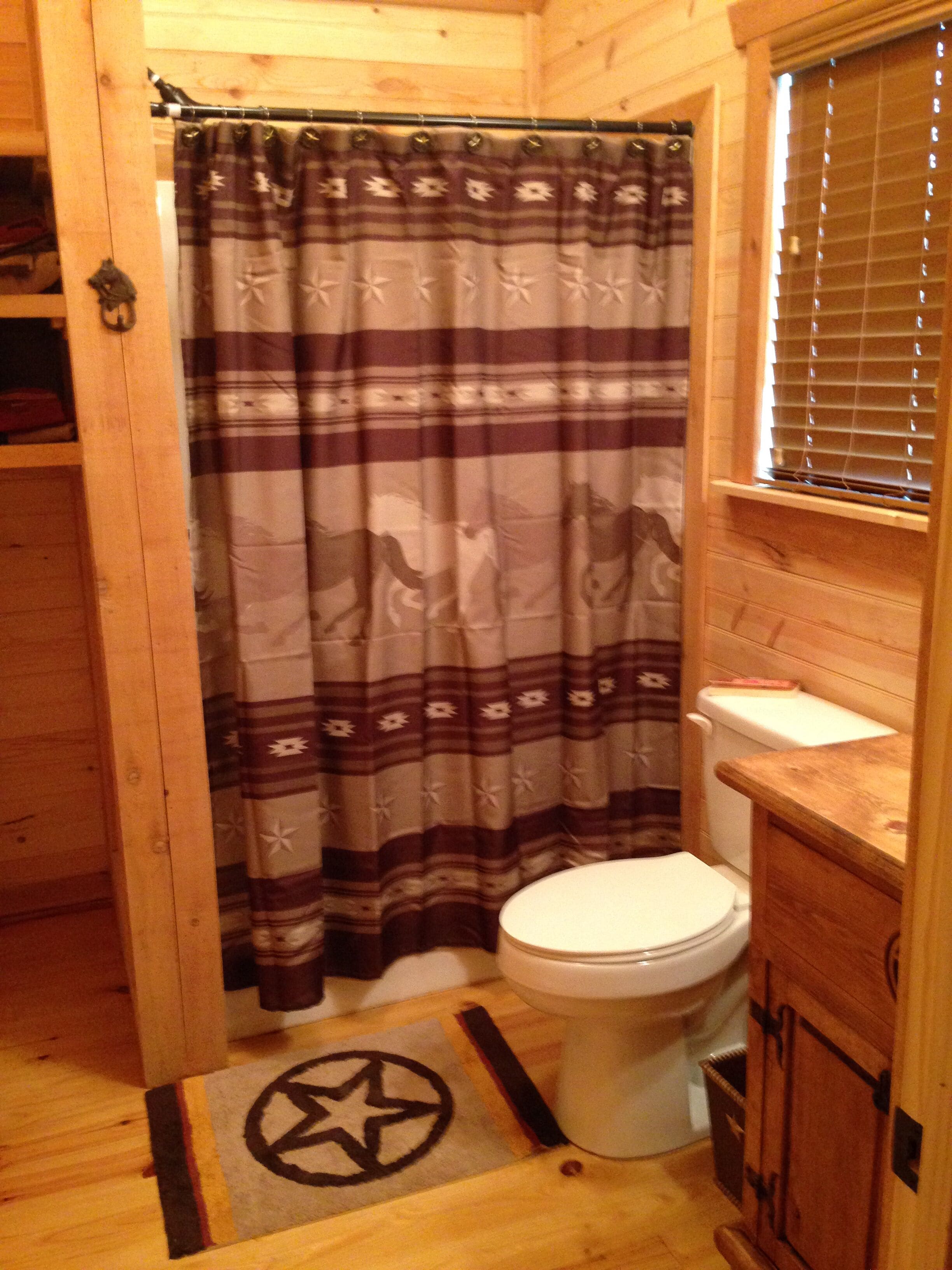 A wooden cabin bathroom with a striped shower curtain, a white toilet, and a wooden vanity.