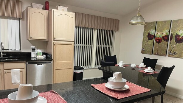 Een moderne keuken met een zwart aanrecht, houten kastjes en een eethoek met een glazen tafel en stoelen.