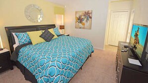 Een slaapkamer met een bed, nachtkastje, dressoir, televisie en een deur.