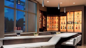 Un espace bar moderne doté d’un long comptoir, de nombreux tabourets et d’un présentoir bien éclairé pour les boissons alcoolisées.