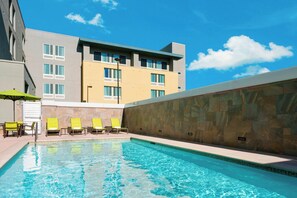 Una piscina con agua azul cristalina, rodeada por un muro de piedra y un edificio con varias ventanas.