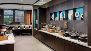 Une cuisine d’hôtel moderne dotée d’un espace buffet, de sièges au bar et d’une grande fenêtre laissant entrer la lumière naturelle.