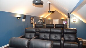 Una sala de cine en casa con varios sillones de cuero negro, un ventilador de techo y un proyector.