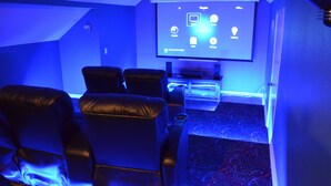 Una sala de cine en casa con una pantalla de proyector mostrando una interfaz multimedia, sillones de cuero reclinables y suelo alfombrado.