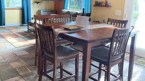 A dining area with a wooden table and chairs, a chandelier, and a television on the wall. - Friendly Reeder Lake House (Kasilof)