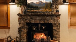 Une cheminée en pierre surmontée d’un téléviseur, encadrée de volets en bois, et une table avec des verres et un saladier.