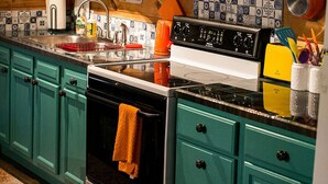 A kitchen with teal cabinets, a stove, and various kitchen items on shelves. - Climb On Inn ~Explore Red River Gorge & Comfort ~Perfect Location ~Pet Friendly  (Pine Ridge)