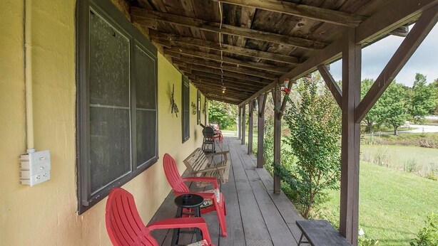 A covered porch with red chairs and a table, a window with shutters, and a grassy yard in the background. - Climb On Inn ~Explore Red River Gorge & Comfort ~Perfect Location ~Pet Friendly  (Pine Ridge)