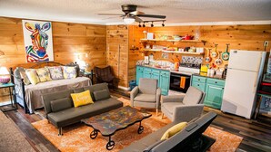 A cozy living room with a sofa, armchairs, and a coffee table. A kitchen with teal cabinets and a refrigerator is visible. - Climb On Inn ~Explore Red River Gorge & Comfort ~Perfect Location ~Pet Friendly  (Pine Ridge)
