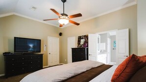 Un dormitorio con cama, televisor, ventilador de techo y cómoda.