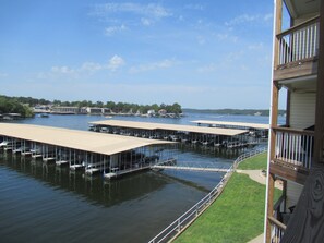 A waterfront property with multiple docked boats, a covered boat launch area, and a grassy deck. -  UPDATED LAKEFRONT WALK-IN UNIT, 2 POOLS, BEACH, DECK (Osage Beach)