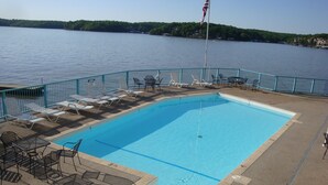 A swimming pool with lounge chairs and tables, surrounded by a blue fence, overlooking a body of water. -  UPDATED LAKEFRONT WALK-IN UNIT, 2 POOLS, BEACH, DECK (Osage Beach)