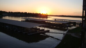 A waterfront property with a dock extending into the water, covered structures, and a clear view of the sunset over the water. -  UPDATED LAKEFRONT WALK-IN UNIT, 2 POOLS, BEACH, DECK (Osage Beach)