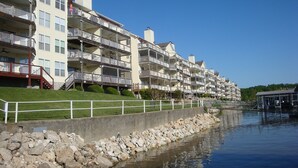 A waterfront residential building with multiple balconies, a grassy area, and a rocky shoreline. -  UPDATED LAKEFRONT WALK-IN UNIT, 2 POOLS, BEACH, DECK (Osage Beach)