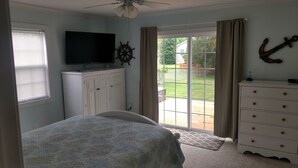 A bedroom with a bed, a dresser, a TV, and a view of the backyard through a sliding glass door. - Quiet convenient location! Remodeled 4br 3ba. Dog friendly, huge deck, hot tub . (Ocean View)