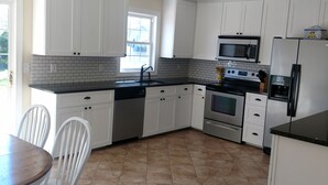 A modern kitchen with white cabinets, a black countertop, and a tiled floor. - Quiet convenient location! Remodeled 4br 3ba. Dog friendly, huge deck, hot tub . (Ocean View)
