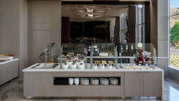 Eine moderne Frühstückstheke mit verschiedenen Speisen und Besteck, einer Kaffeemaschine und Blick ins Freie.