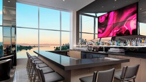 Zona de bar moderna con una gran pantalla de televisión, taburetes y vistas a una masa de agua.