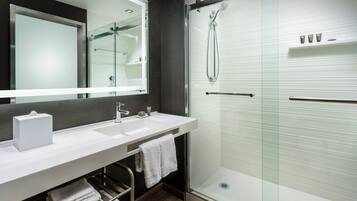 A modern bathroom with a large mirror, two sinks, a glass shower enclosure, and a towel rack.