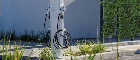 A power charging station with cables, located outdoors near a building with a blue wall and green plants.