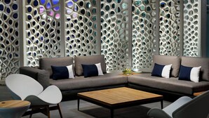Una sala de estar moderna con un sofá modular, dos sillones, una mesa de centro y una pared decorativa con motivos geométricos.