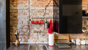 A kitchen with a brick wall, stainless steel sink, and hanging utensils. - Loft 1910 - Kazimierz Echoes (Kraków)
