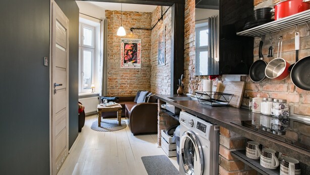 A modern kitchen with a brick wall, a washing machine, and a dining area with a sofa and table. - Loft 1910 - Kazimierz Echoes (Kraków)