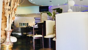 Un hall d’hôtel moderne comprenant un comptoir d’accueil, un espace salon et des éléments décoratifs tels qu’un vase et des plantes.