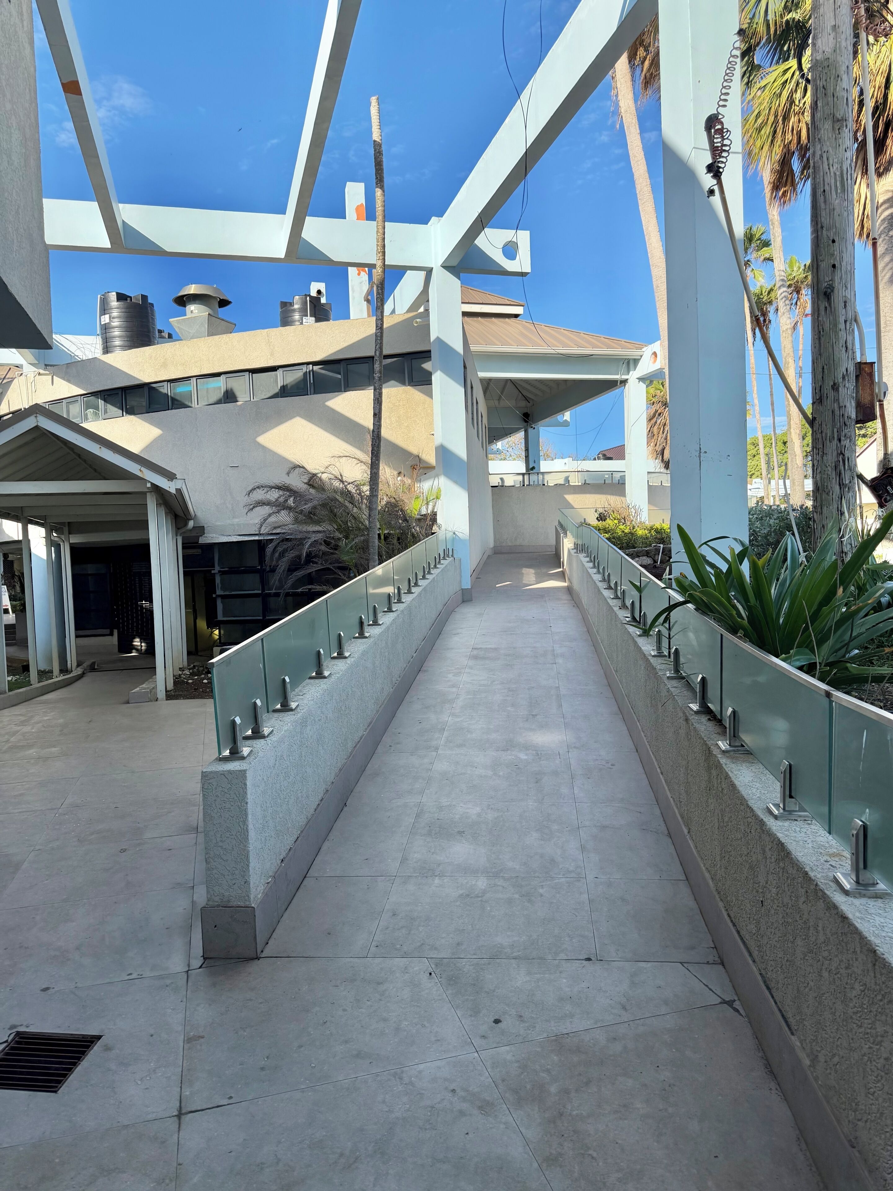 Un pasillo cubierto con piso de concreto, barandales metálicos y vistas a un edificio de estilo arquitectónico moderno.