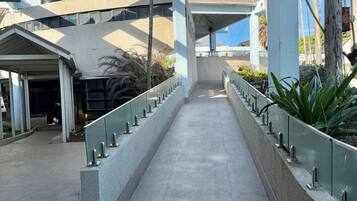 Un pasillo cubierto con piso de concreto, barandales metálicos y vistas a un edificio de estilo arquitectónico moderno.