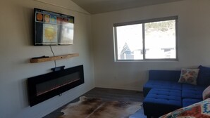 A living room with a mounted TV, a blue sofa, a patterned throw blanket, and a large fur rug. - Downtown Pagosa Springs, within walking distance to everything (Pagosa Springs)