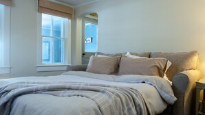 A bedroom with a bed, a nightstand, a window with curtains, and a door.