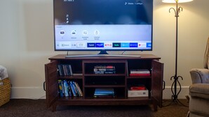 A flat-screen TV on a wooden stand with a remote control, a lamp, and a bookshelf with books and DVDs.