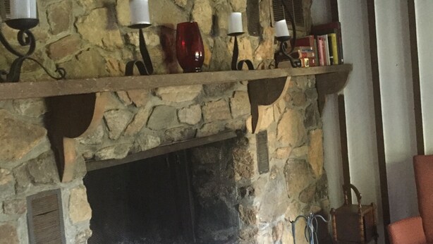 Una chimenea de piedra con repisa que sostiene velas y libros, una silla y una reja de protección.