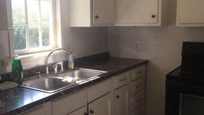 Una cocina con armarios blancos, encimera negra, pileta de acero inoxidable y ventana con vista a la vegetación.