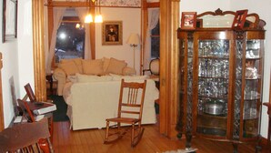 Une pièce chaleureuse avec un fauteuil à bascule en bois, un canapé, une vitrine contenant de la vaisselle et un lustre.